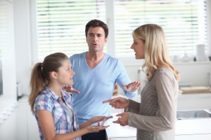 Mid adult woman arguing with daughter in kitchen as father tries to settle dispute