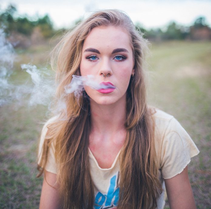 Woman vaping outside on grassy field