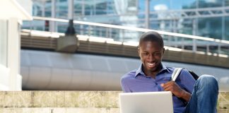 Portrait of young man sitting outdoors and using laptop