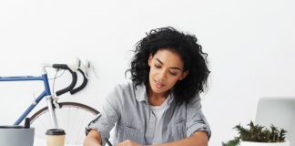 Smiling young self-employed woman architect making drawing at her home office using pen, excited about working process