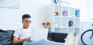 Handsome Asian man using laptop on sofa at home