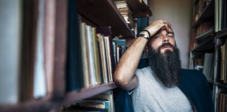 Thoughtful hipster man among bookshelves. Depression concept