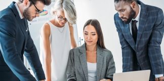 Businesspeople standing around team leader and looking at documents