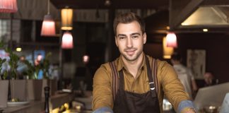 Attractive young barista with cup of delicious coffee looking at camera