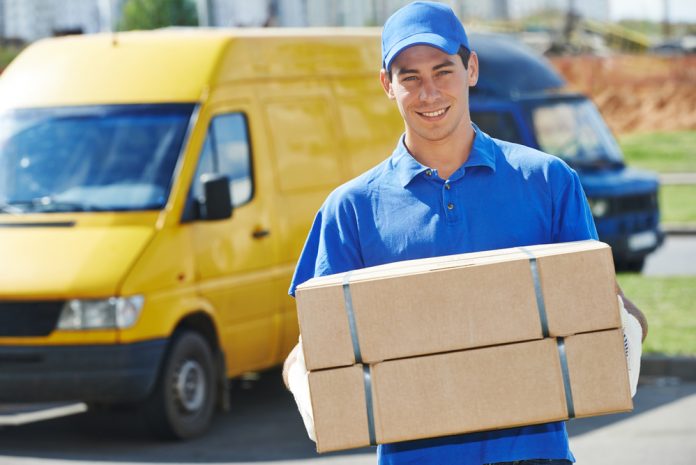 Smiling young male postal delivery courier man in front of cargo van delivering package