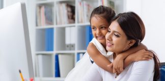 Business lady working on computer while her daughter hugs her