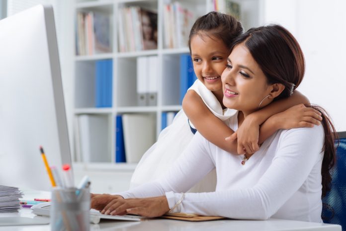 Business lady working on computer while her daughter hugs her