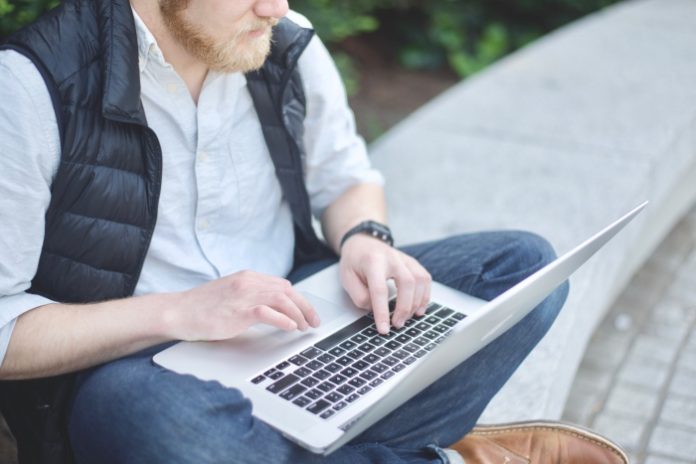 Man sitting on ground and typing on laptop