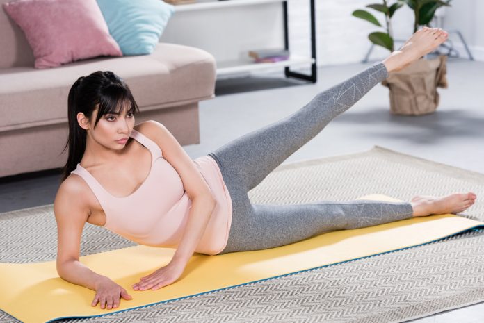 Woman lying on yoga mat and lifting leg at home
