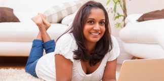 Young happy woman lying down on the floor and using laptop