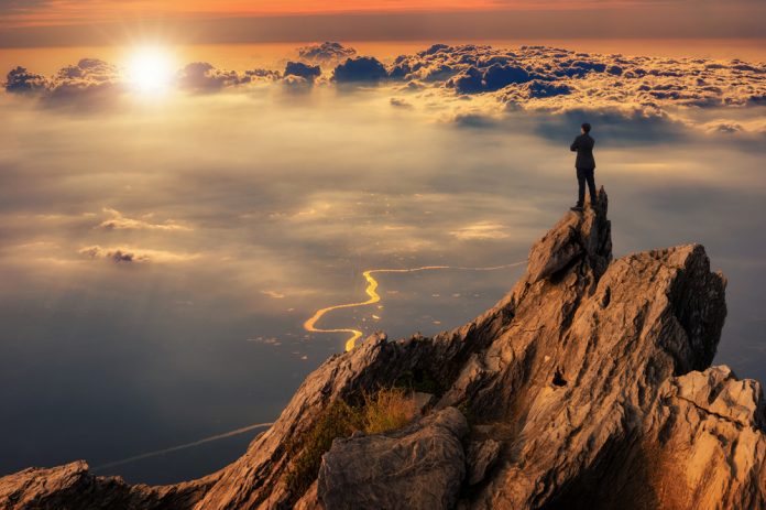 Businessman wearing comfortable casual suit jacket standing on top of peak mountain and looking forward