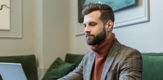 Handsome bearded businessman in formal wear sitting at table and typing on laptop in restaurant