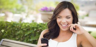 Smiling Young Adult Female Texting on Cell Phone Outdoors on a Bench