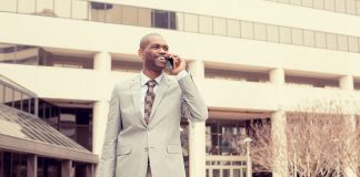 Young busy happy, smiling business man talking on mobile phone holding briefcase walking down the street outside corporate office isolated on city background