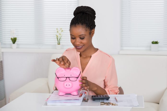 Smiling Woman Inserting Coin In Piggy Bank