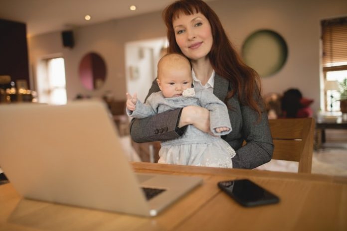 Woman holding baby and working at laptop