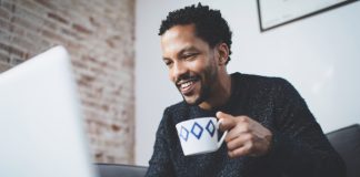 Cheerful man using computer and smiling while sitting on the sofa