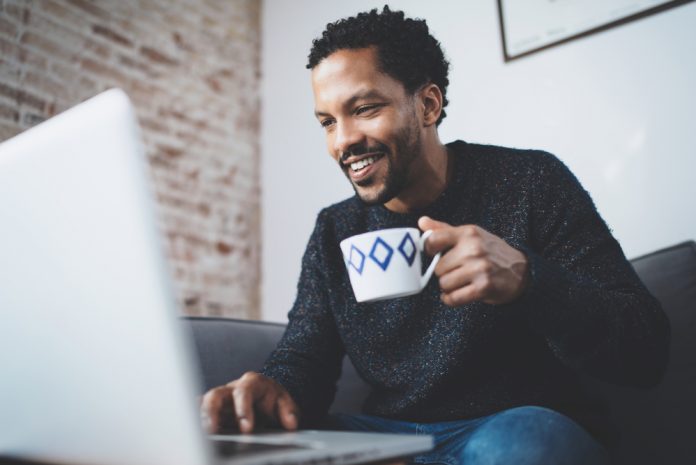 Cheerful man using computer and smiling while sitting on the sofa