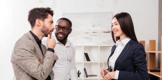 Businessmen and businesswoman standing near table and happily talking while working together in office