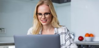 Smiling woman in eyeglasses using laptop while working at home