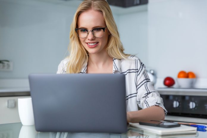 Smiling woman in eyeglasses using laptop while working at home
