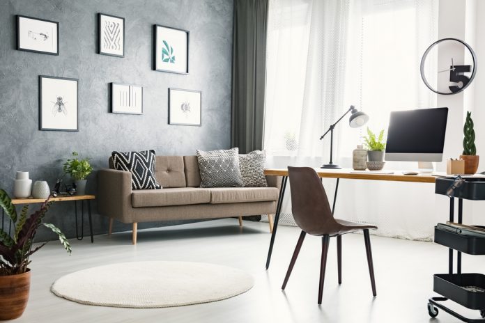 Bright home office interior with a sofa, graphics, desk with a computer and lamp and modern clock