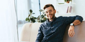 Smiling man in eyeglasses with laptop sitting on sofa at home