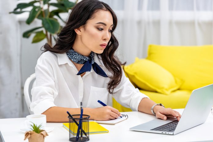 Attentive freelancer using laptop and writing in notebook