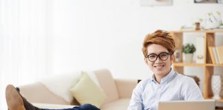 Cheerful man keeping his feet on the table when working on laptop at home