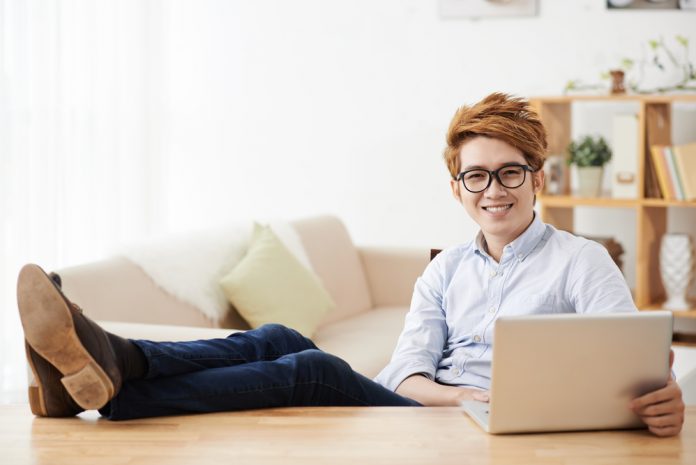 Cheerful man keeping his feet on the table when working on laptop at home
