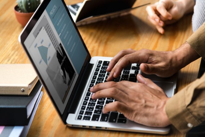 Businessperson typing on laptop while colleague watches