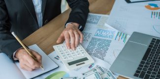 Financier using calculator and writing something in notebook in office