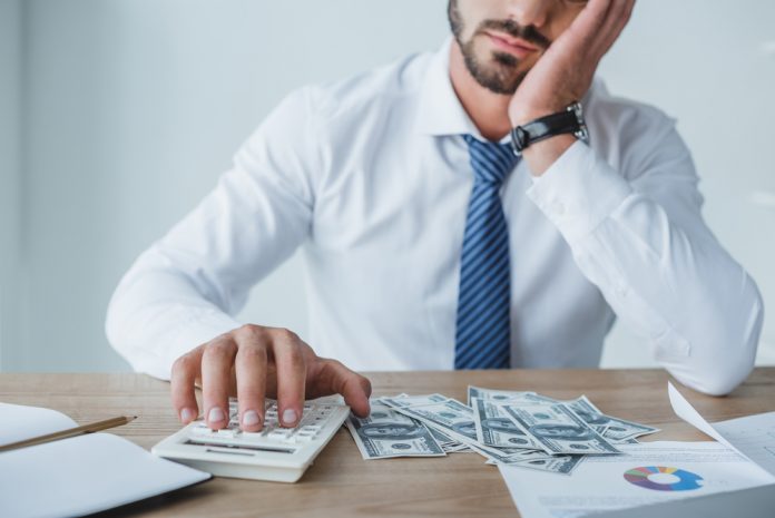 Tired financier counting money with calculator in office