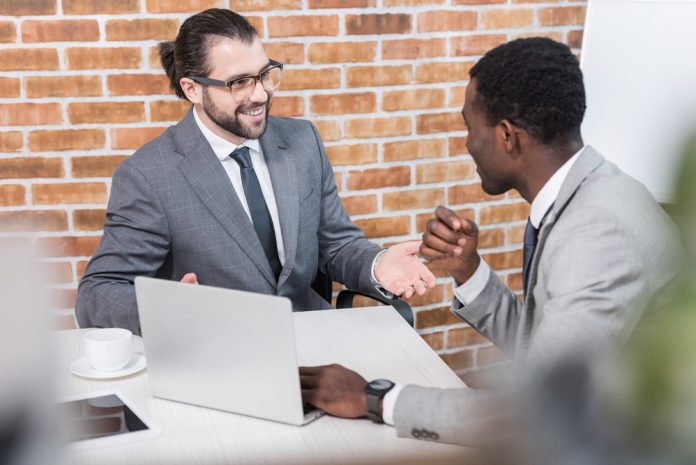 Businessmen smiling and talking at table with laptop