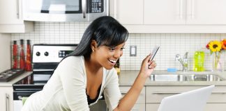 Smiling woman online shopping using computer and credit card in kitchen