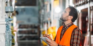 Male worker in safety vest writing in notepad in storehouse