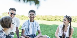 Happy students sitting on grass and studying together in park