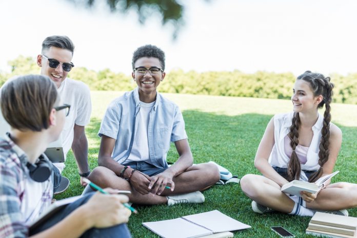 Happy students sitting on grass and studying together in park