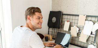 Young smiling man using laptop at desk in home office