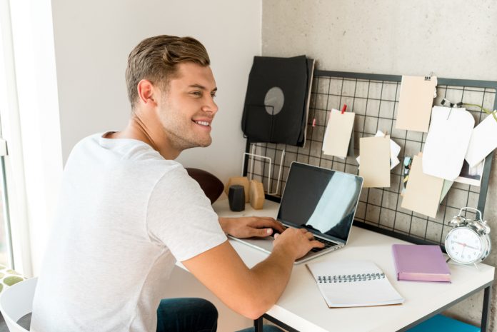 Young smiling man using laptop at desk in home office