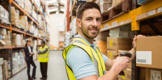 Warehouse worker scanning box while smiling at camera in a large warehouse