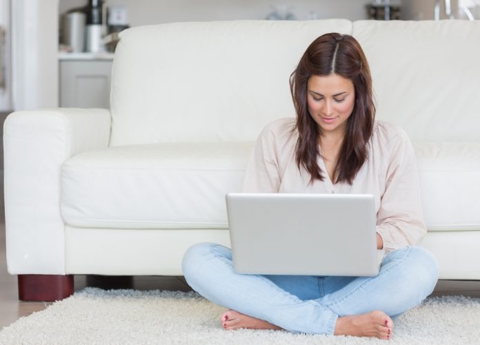 Woman sitting on the carpet typing on her laptop
