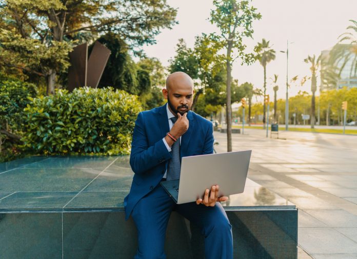 Businessman holding laptop notebook wearing blue suit near office