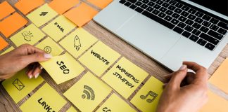 Woman touching sticky note with SEO lettering near laptop on desk