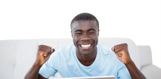 Cheering man sitting on couch using laptop