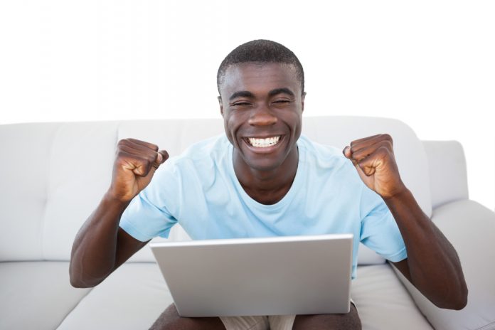 Cheering man sitting on couch using laptop