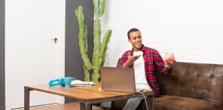 Man with laptop in living room holding a big piggybank