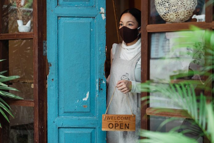 Woman wearing face mask opening shop