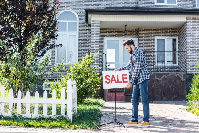 Person Putting Sale Sign in Front of House