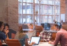 A startup team sits in a conference room with orange chairs and glass walls. They're all at the table talking.